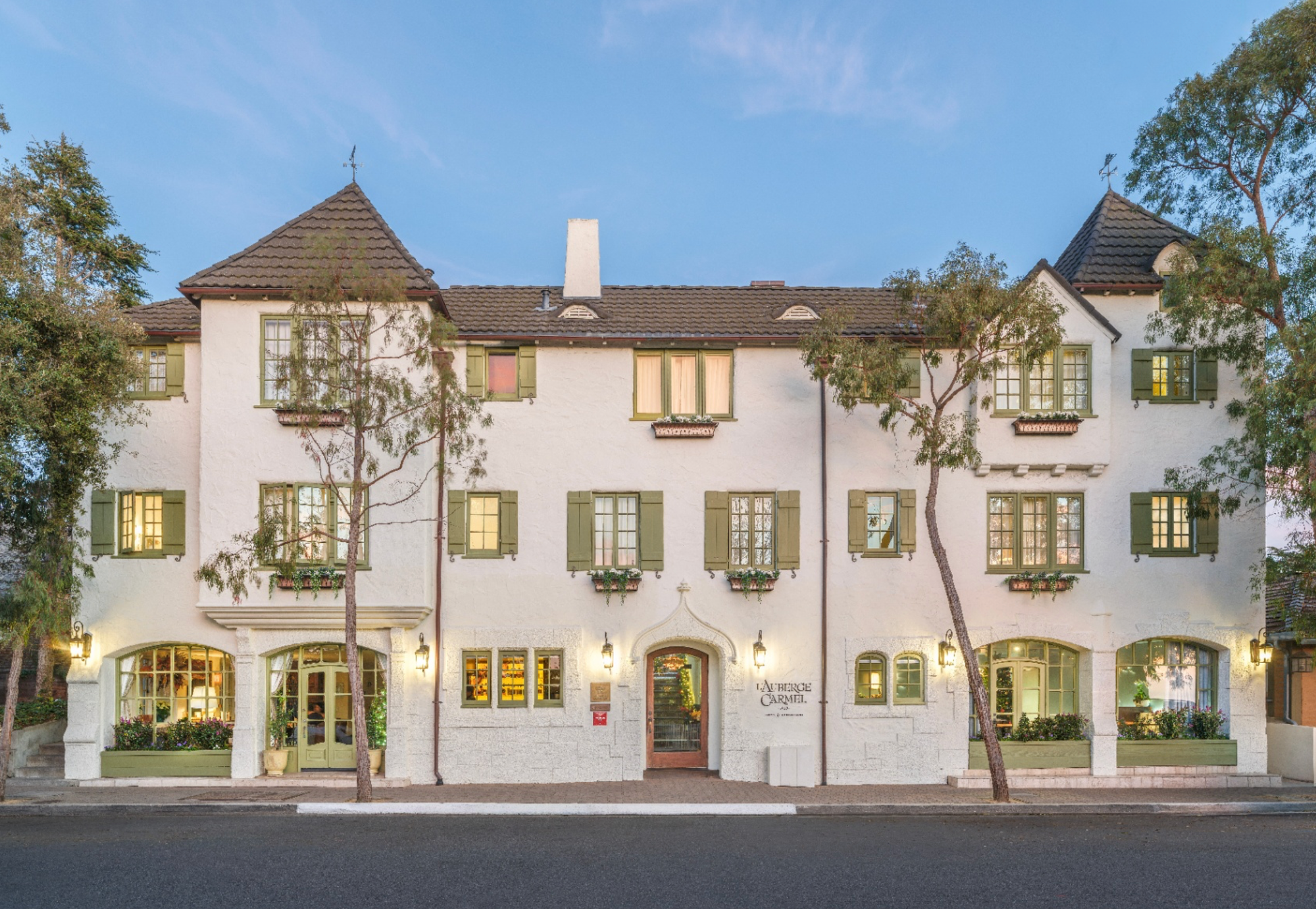 The whitewashed exterior of L’Auberge Carmel beneath a clear blue sky
